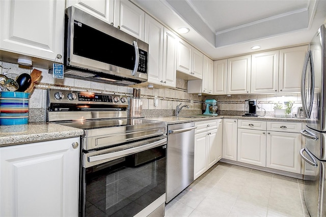 kitchen with stainless steel appliances, white cabinets, decorative backsplash, a sink, and crown molding