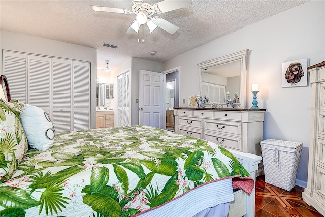 bedroom with a textured ceiling, ensuite bathroom, a ceiling fan, and multiple closets