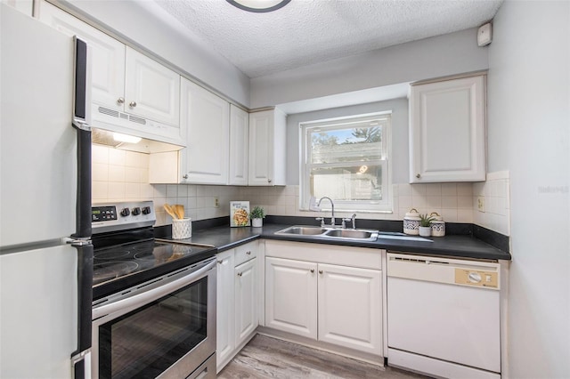 kitchen with a sink, dark countertops, white cabinetry, white appliances, and under cabinet range hood