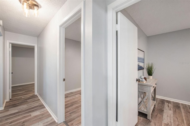 corridor featuring a textured ceiling, baseboards, and wood finished floors