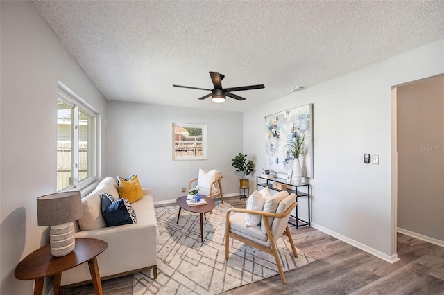 living area with light wood-style floors, visible vents, a ceiling fan, and a textured ceiling