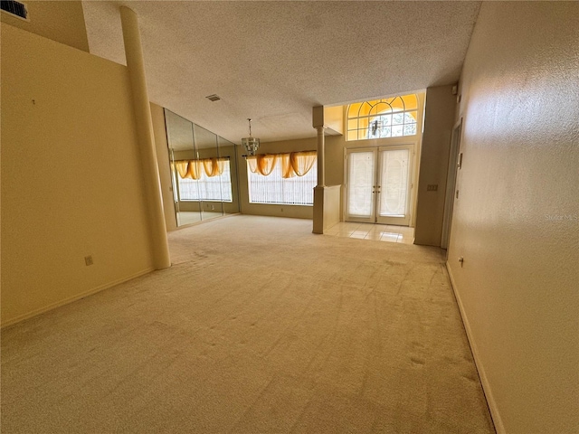 interior space with french doors, a textured ceiling, visible vents, baseboards, and light carpet
