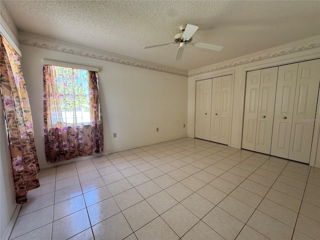 unfurnished bedroom featuring ceiling fan, a textured ceiling, light tile patterned floors, and multiple closets