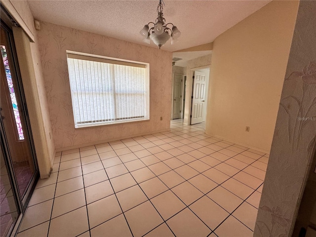 empty room with a textured ceiling, plenty of natural light, light tile patterned floors, and a notable chandelier