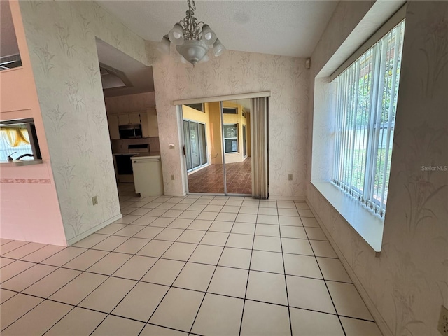 empty room with a chandelier, wallpapered walls, and light tile patterned flooring
