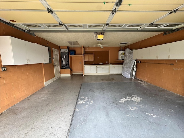 garage with heating unit, water heater, concrete block wall, and a garage door opener