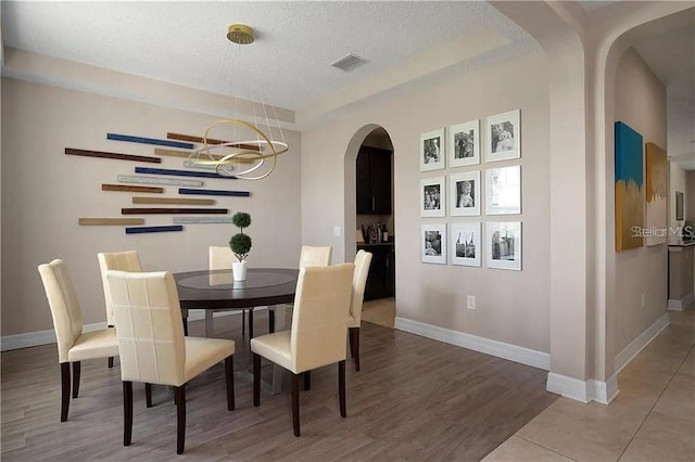 4407 Scarlet Loop, Wesley Chapel, FL 33544 - dining room featuring a textured ceiling, a chandelier, baseboards, arched walkways, and wood finished floors