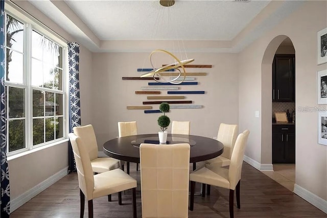 4407 Scarlet Loop, Wesley Chapel, FL 33544 - dining room featuring baseboards, arched walkways, light wood-style flooring, and a tray ceiling