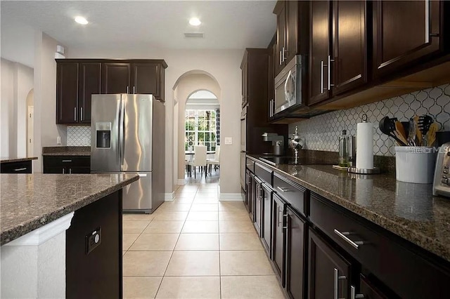 4407 Scarlet Loop, Wesley Chapel, FL 33544 - kitchen with appliances with stainless steel finishes, arched walkways, dark brown cabinetry, and light tile patterned flooring
