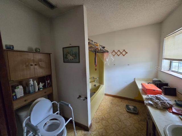 full bath with toilet, a textured ceiling, visible vents, tub / shower combination, and baseboards