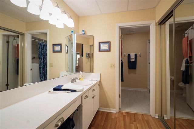 full bath featuring toilet, wood finished floors, a notable chandelier, baseboards, and vanity