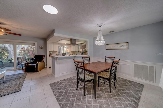 dining room with light tile patterned floors, a ceiling fan, wainscoting, a textured ceiling, and a chandelier