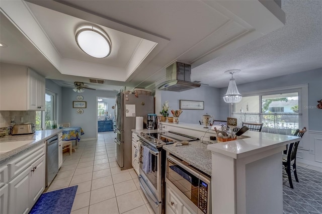 kitchen with ventilation hood, appliances with stainless steel finishes, a tray ceiling, white cabinets, and light tile patterned flooring