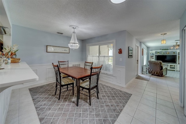 dining room featuring light tile patterned flooring, a chandelier, wainscoting, a textured ceiling, and a decorative wall