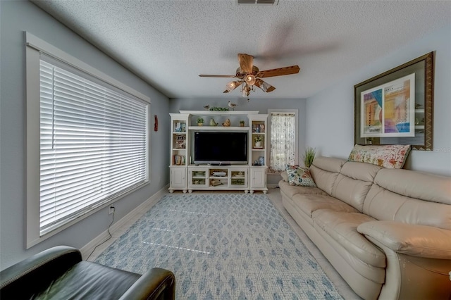 living area with a ceiling fan, healthy amount of natural light, baseboards, and a textured ceiling