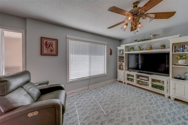 living area featuring ceiling fan, a textured ceiling, and baseboards