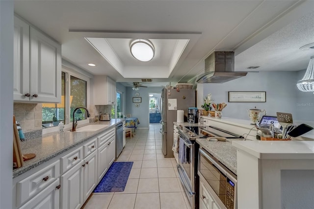 kitchen featuring range hood, stainless steel appliances, a sink, white cabinets, and a tray ceiling