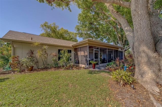rear view of property featuring a sunroom, a lawn, and stucco siding