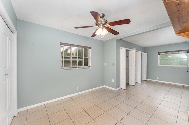 unfurnished bedroom featuring ceiling fan, baseboards, a closet, and light tile patterned floors