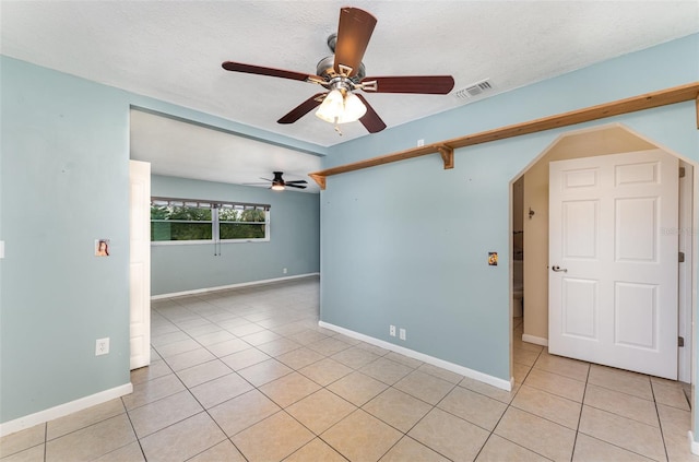empty room featuring light tile patterned flooring, baseboards, a ceiling fan, and visible vents