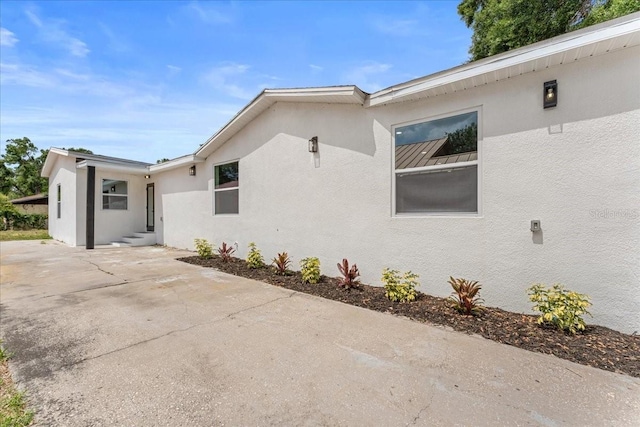 3215 E Powhatan Ave, Tampa, FL 33610 - view of side of home with stucco siding, entry steps, a standing seam roof, a patio, and concrete driveway
