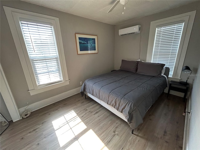 bedroom with wood finished floors, baseboards, and a wall mounted AC