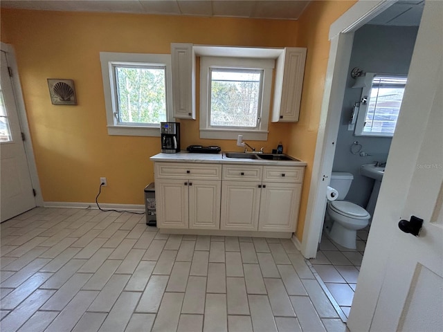 kitchen with baseboards, light countertops, white cabinets, and a sink