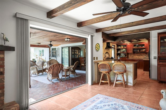 dining space with a ceiling fan, beam ceiling, light tile patterned flooring, and wet bar