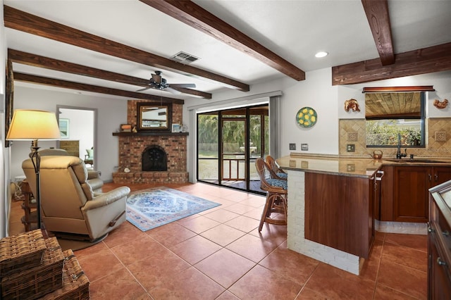 living area featuring plenty of natural light, a brick fireplace, ceiling fan, tile patterned floors, and beam ceiling