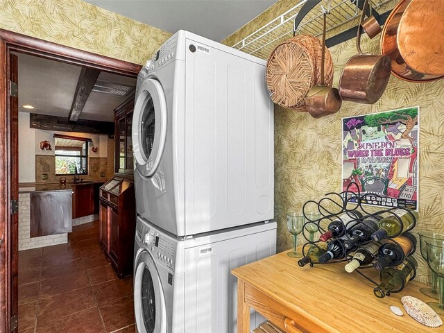 laundry room with stacked washer / drying machine, wallpapered walls, and dark tile patterned flooring