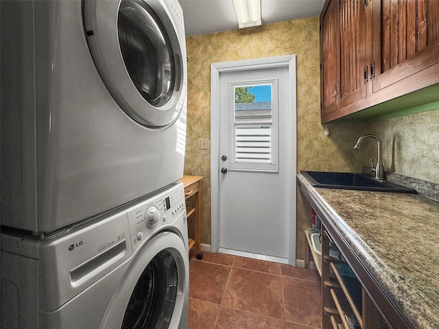 laundry room featuring stacked washer / drying machine, dark tile patterned flooring, baseboards, and cabinet space