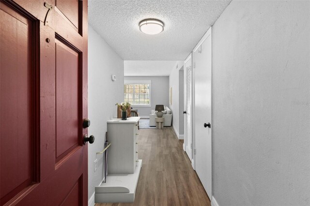 hall featuring wood finished floors, a textured ceiling, and baseboards
