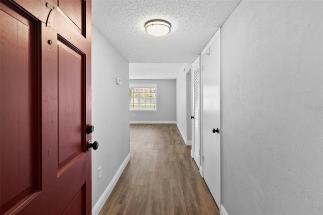 corridor with wood finished floors, baseboards, and a textured ceiling