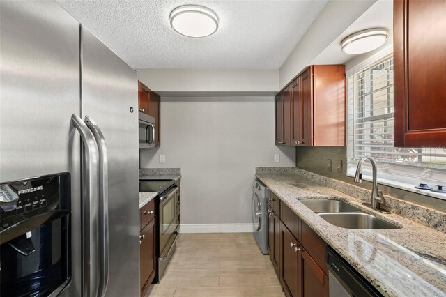 kitchen featuring appliances with stainless steel finishes, a sink, washer / clothes dryer, baseboards, and light stone counters