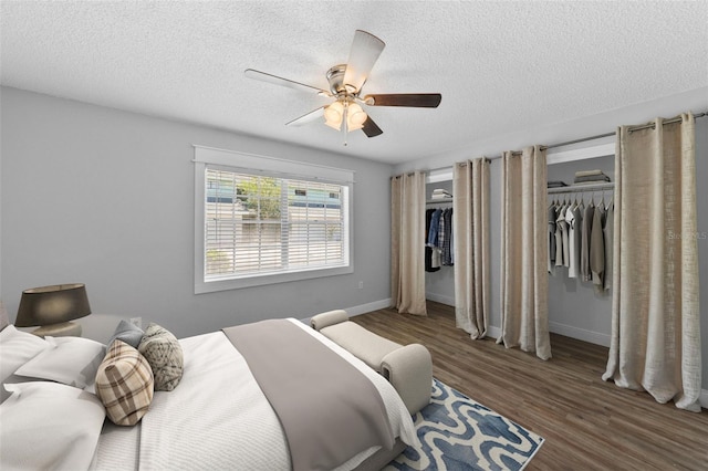 bedroom with multiple closets, wood finished floors, a textured ceiling, baseboards, and a ceiling fan