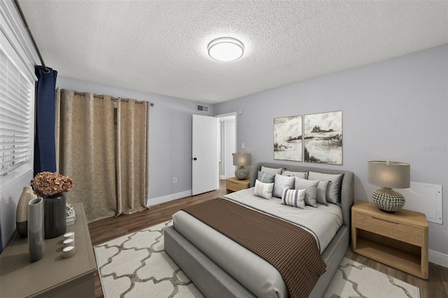 bedroom with wood finished floors, a textured ceiling, and baseboards