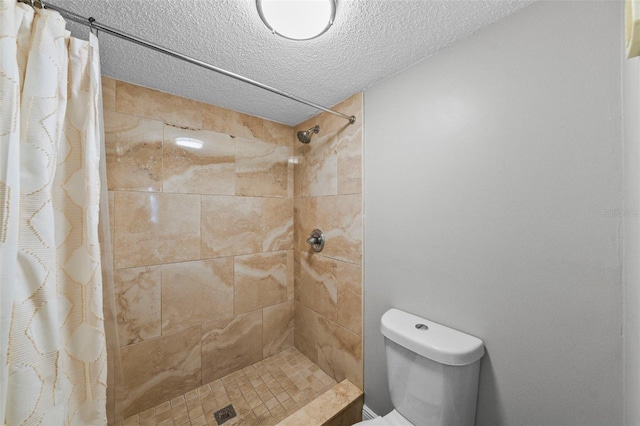 bathroom featuring a tile shower, toilet, and a textured ceiling