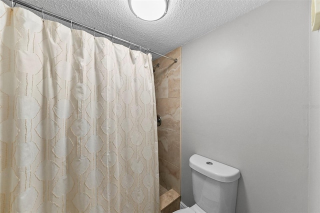full bath featuring a textured ceiling, a tile shower, and toilet