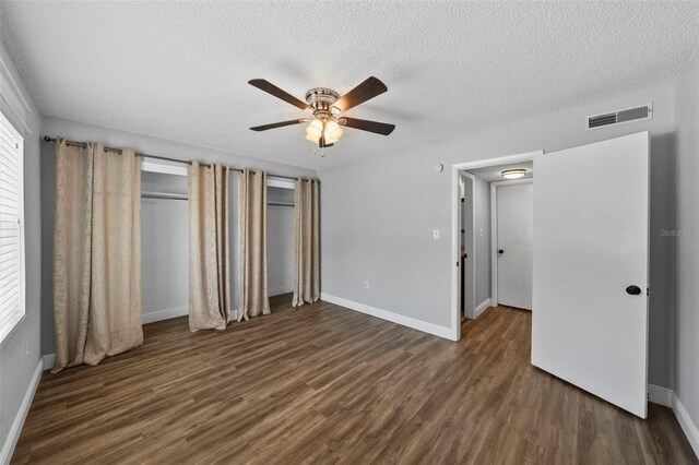 unfurnished bedroom with wood finished floors, baseboards, a textured ceiling, a ceiling fan, and multiple closets