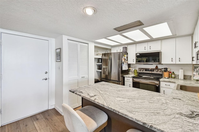 500 Treasure Island Cswy Unit 607, Treasure Island, FL 33706 - kitchen with appliances with stainless steel finishes, a peninsula, light wood finished floors, white cabinetry, and a textured ceiling