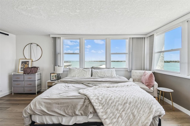 500 Treasure Island Cswy Unit 607, Treasure Island, FL 33706 - bedroom with a water view, wood finished floors, a textured ceiling, and baseboards