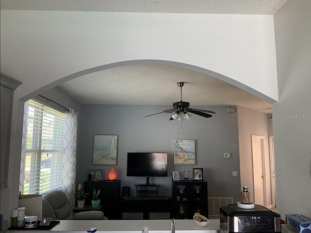 living room with arched walkways, ceiling fan, and a textured ceiling