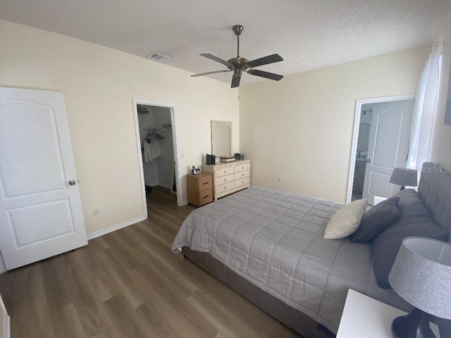 bedroom with a walk in closet, wood finished floors, a textured ceiling, a closet, and a ceiling fan