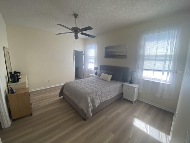 bedroom featuring a textured ceiling, light wood finished floors, baseboards, and a ceiling fan