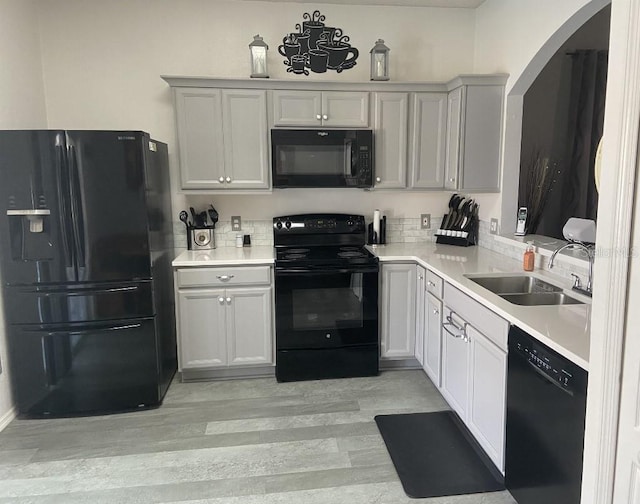 kitchen featuring black appliances, a sink, light countertops, light wood-style flooring, and arched walkways