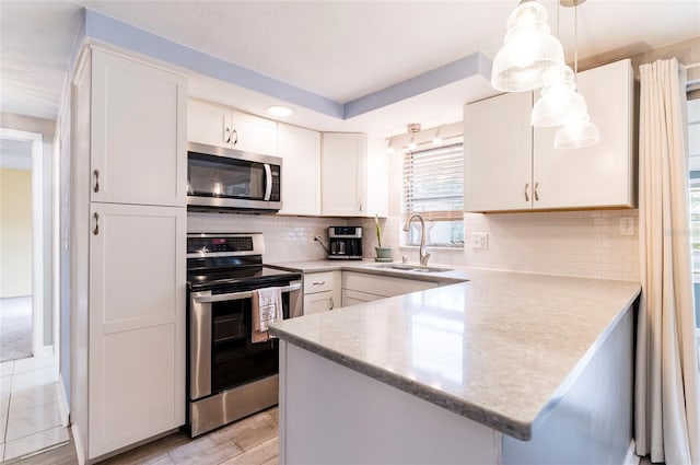 kitchen featuring appliances with stainless steel finishes, a sink, a peninsula, white cabinetry, and light wood-style flooring