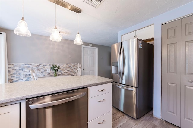 kitchen featuring appliances with stainless steel finishes, light countertops, backsplash, white cabinetry, and light wood-style floors