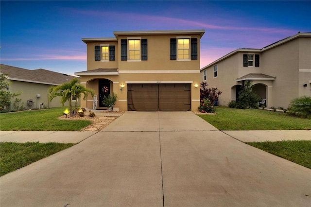 traditional-style home with stucco siding, a garage, concrete driveway, and a yard