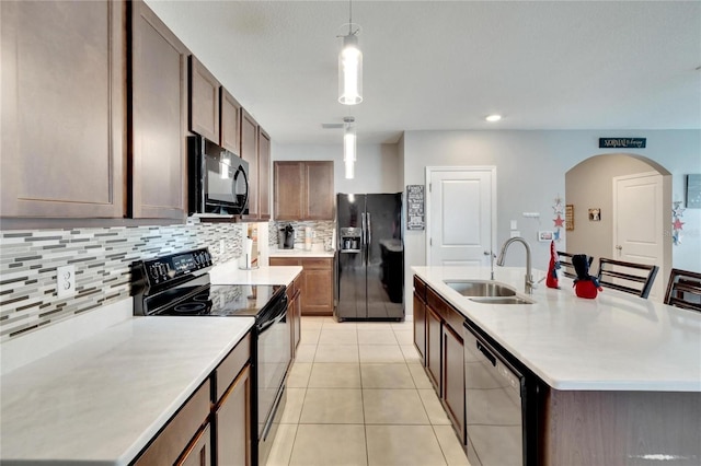 kitchen featuring black appliances, a sink, backsplash, light countertops, and a kitchen island with sink