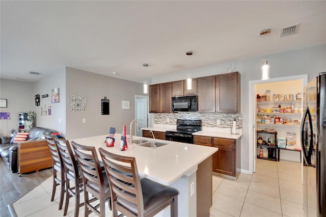 kitchen featuring black appliances, a sink, light countertops, a kitchen bar, and decorative backsplash